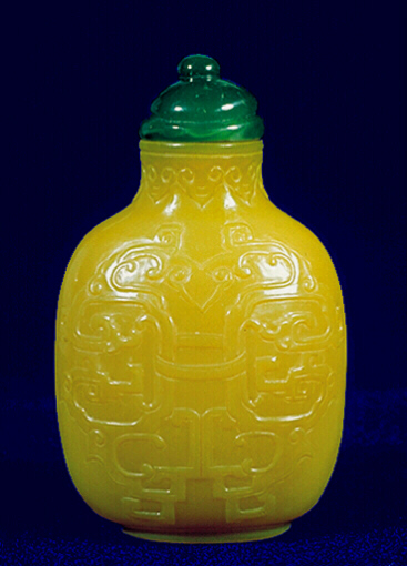 A carved Imperial yellow glass snuff bottle, carved on each face with an identical scene of confronting archaic dragons, linked together with bands at the central and lower areas, the neck surrounded with ruyi lappets.