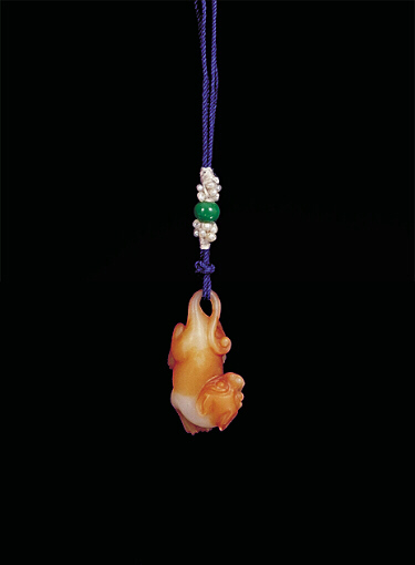 Nephrite pendant, pale white with darker brown areas carved in miniature form showing a reclining dog, its head pointing backwards and its tale looped to receive the cord.