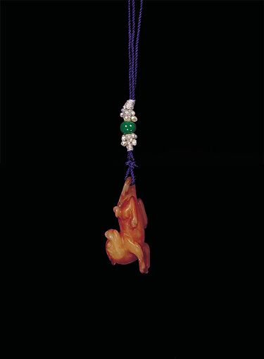 Reverse: Nephrite pendant, pale white with darker brown areas carved in miniature form showing a reclining dog, its head pointing backwards and its tale looped to receive the cord.