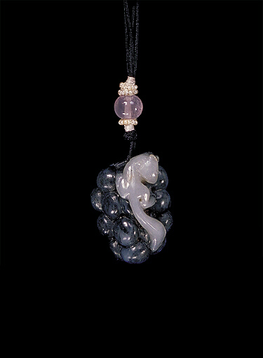 Nephrite pendant, mutton fat with a large dark grey area, carved in the form of a squirrel that is scampering over a bunch of grapes with leaves.