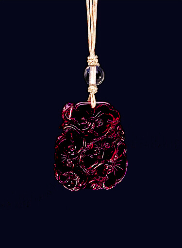 Glass pendant of dark red colour imitating amber carved with a formalised design of ruyi fungus throughout, the base with a bat on one corner. Imperial Palace Workshops, Beijing.