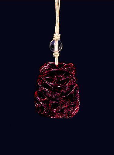 Reverse: Glass pendant of dark red colour imitating amber carved with a formalised design of ruyi fungus throughout, the base with a bat on one corner. Imperial Palace Workshops, Beijing.